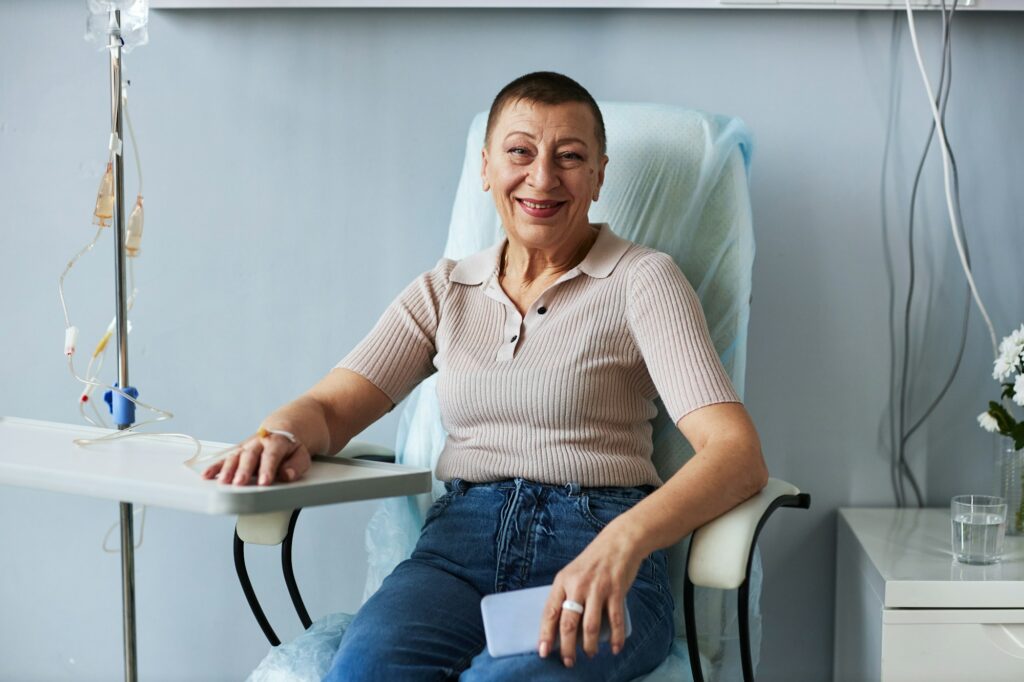 Smiling mature woman looking at camera during IV drip treatment in clinic